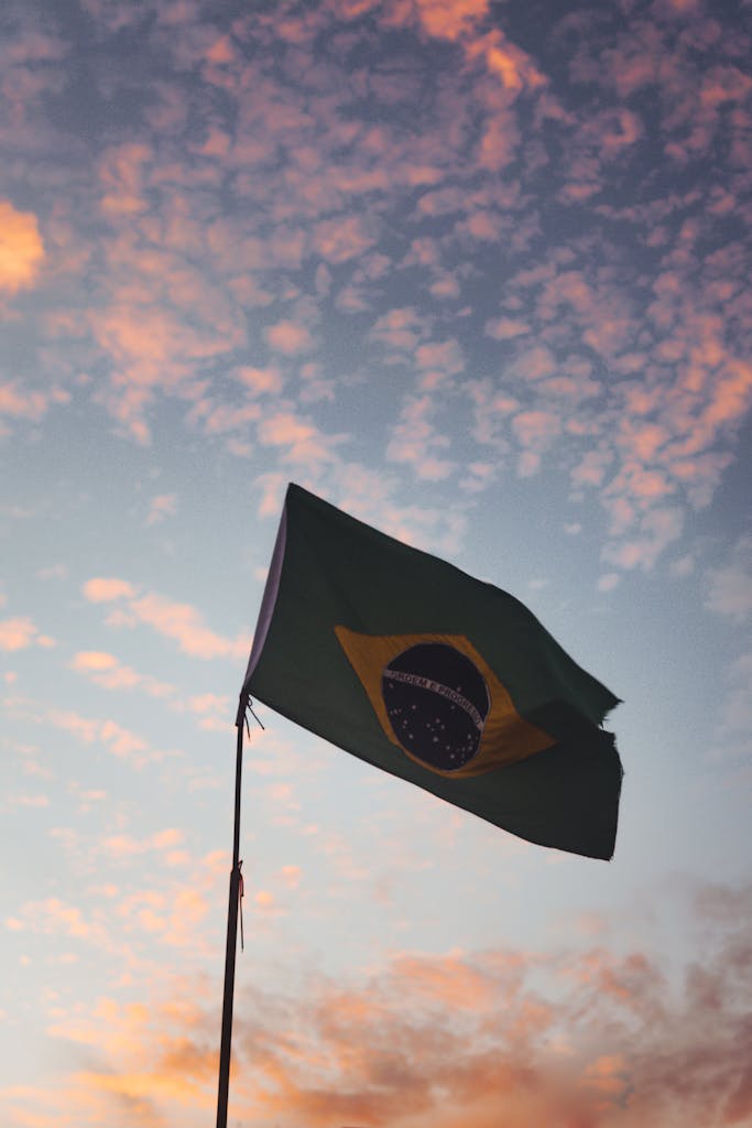 bandeira brasileira contra um vibrante céu de pôr do sol, simbolizando orgulho nacional e liberdade